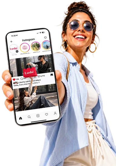 A smiling woman holding up a phone showing Lushé on Instagram